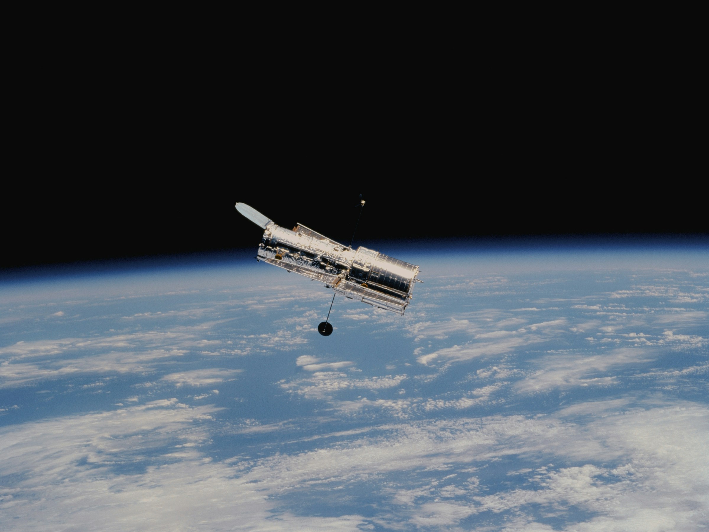 Hubble Space Telescope with Earth in the background looking out towards the universe.