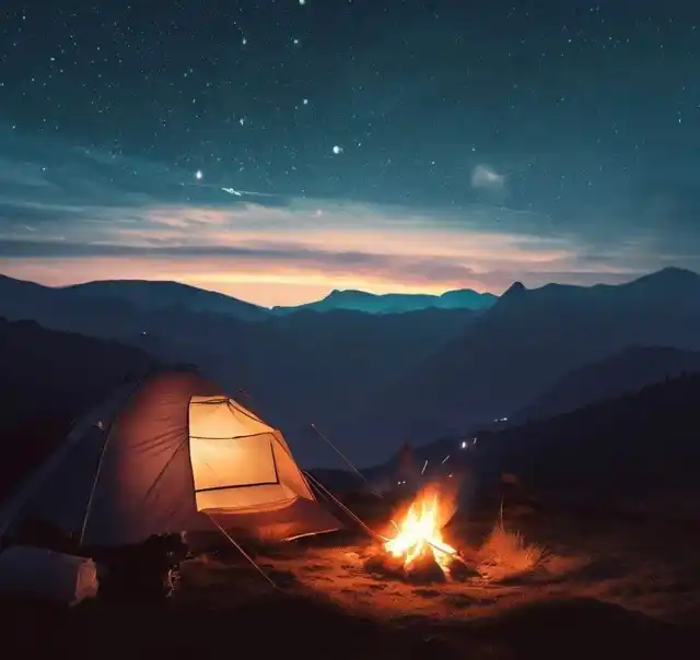A tent on a hilltop with fire burning nearby and the milky way visible in the skies.